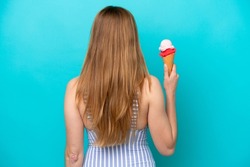 Young caucasian woman in swimsuit eating ice cream isolated on blue background in back position