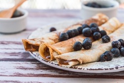 Delicious plate with homemade pancakes or crepes filled with dulce de leche and blueberries and icing sugar covering the plate.