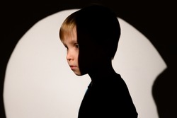 Emotions. Portrait of a child. A harsh harsh light falls on the face, a circle from the lamp is visible on the background. The sad, serious face of a child.