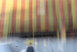 Blurry human figure next to corrugated fence with under construction sign and striped debris netting draped building. Intentional camera movement abstract street photography.