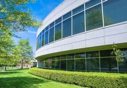 Green hedge and mowed lawn along round shaped wall of the office building