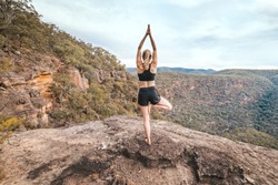 Female yoga exercise fitness. She is balancing on one leg standing on a cliff ledge overlooking the gorge junctions.Wollemi National Park