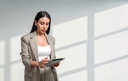 Office woman in beige suit concentrated, working with device. Office company and staff. Copy space blank wall. Concept of boss and management