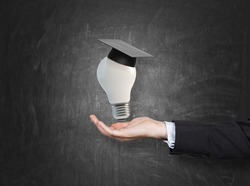 A hand holding a mortarboard with a light bulb, concept of education. 