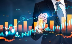 Businessman with pen point at stock market diagrams, hologram with bar chart and growing lines. Numbers and dynamic changes. Concept of financial analysis
