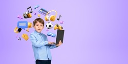 Serious little boy kid holding laptop standing over purple background with online entertainment and gaming icons around him. Concept of modern technology. Copy space