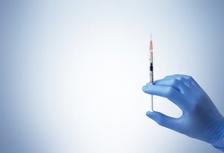 A hand in a blue medicine glove with a disposable syringe. Blue background.
