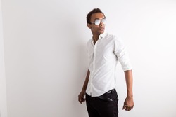 Stylish african american guy in sunglasses and formal outfit posing for camera on light background with copy space