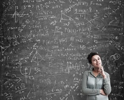 Portrait of African American woman solving a difficult task standing near blackboard with formulas. Concept of science. Mock up