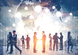 Silhouettes of business people shaking hands and walking against a morning cityscape. There is a world map and a network.  Elements of this image furnished by NASA. Toned image. Double exposure.
