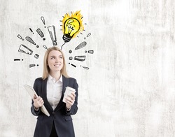 Portrait of a positive blond woman standing near a concrete wall with a light bulb drawing surrounded by exclamation marks on it. Mock up