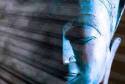 Buddha face close-up. Spiritual enlightenment. Zen Buddhism. Traditional Thai statue with ethereal light. Peaceful blue tone meditation image. Awakening the mind of self with Buddhist mindfulness.