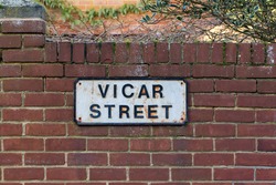 Vicar Street sign. Religious career path. Road leading to the church manse. Spiritual direction of an English town place name fixed to a red brick garden wall. Honest job and pious life of devotion