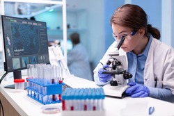 Scientist looking into microscope in virus research laboratory with pharmacy development equipment. Woman working on science vaccine chemistry experiment in modern lab, analyzing pharmaceutical work