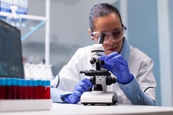 Microbiologist doctor woman analyzing vaccine results using medical microscope researching bacteriology infection diagnostics against coronavirus. Specialist doctor working in biotechnology laboratory