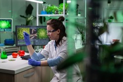 Biologist researcher woman analyzing microscope slide with leaf sample discovering genetically modified botany plant during biological experiment. Biochemist scientist working in biochemistry hospital