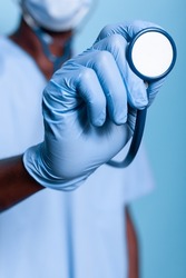 Close up of assistant hand holding stethoscope and wearing gloves against coronavirus pandemic. Nurse with uniform having medical cardiology instrument for heartbeat examination.
