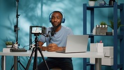 Vlogger recording video on camera with tripod in studio. Influencer using microphone and headphones to film vlog for social media channel. Blogger with equipment filming for podcast.