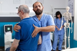 Orthopedic nurse stretching spinal cord and shoulder of elder patient with injury for physiotherapy. Chiropractor giving help to senior man with back pain for physical recovery.