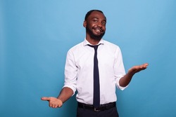 Portrait of smiling businessman with open palms weighing options on blue background. Confident office worker doing hand gesture comparing pros and cons putting decision in balance.