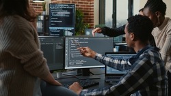 Software developers discussing about source code compiling discovers errors and asks the rest of the team for explanations in front of multiple screens running algorithms. Programmers doing teamwork.