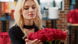 Portrait of romantic beautiful woman smiling and smelling roses feeling in love admiring luxury gift bouquet of roses in living room. Seductive blonde passionate about recieving valentine day flowers.