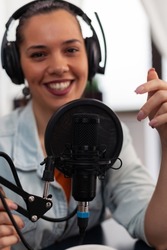Closeup of smiling woman influencer talking into microphone. Vlogger with headphones using recording gear for live broadcast. Audio streaming equipment for internet online radio production.