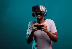 African american guy playing video game with controller and vr headset, enjoying online play with futuristic 3d simulation in studio. Gamer with virtual reality glasses holding joystick.