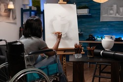 Young illustrator in wheelchair drawing artistic vase ilustration using graphic pencil during paintings lesson in creativity studio. Artist student with disability sketching draw on canvas