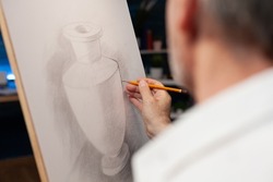 Closeup of original pencil drawing of vase on paper canvas done freehand by elderly man in creative workshop. Detailed view of sketch of still object done by inspired retired artist in home studio.