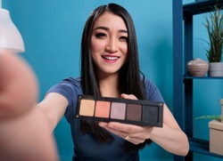 Pov of asian influencer holding makeup palette showing to fans while recording cosmetics review for vlogging channel. Social media creator filming videoblog advertising make up product