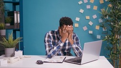 Desperate employee working on laptop computer at desk, feeling tired and stressed about deadline. Overworked man feeling frustrated and disappointed about job mistake. Sad person