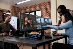 Professional videographer sitting at desk while coworker helping her with film footage visual quality improvement. Video editing expert using multi monitor workstation to edit movie frames.