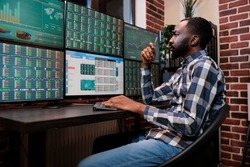 Busy hedge fund trader reviewing financial data and market trend while sitting at workstation. Preocuppied african american broker risking capital in order to analyze fintech company real time charts.