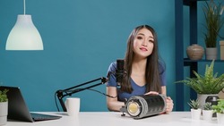 Female blogger recommending studio light accessory on camera, filming online product review with modern lighting equipment. Smiling influencer using broadcast gadget for channel. Tripod shot.