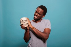 Portrait of young guy holding skull from human skeleton to study genetic scientific brain disease, anatomy and biology education. Anatomical subject to discover science knowledge.
