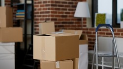 Stacks of cardboard boxes in empty real estate property with furniture, lamp and interior decor. Nobody in living room apartment with carton storage containers and cargo packages. Close up.