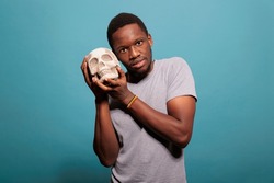 Casual man showing human skull bones in front of camera, studying scientific medicine to learn skeleton knowledge. Young adult holding anatomical subject for biology and anatomy lesson.