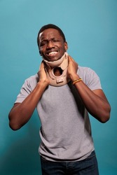 Disappointed adult wearing cervical collar to cure physical injury after sprained bone accident. Young man with neck foam suffering from fractured vertebrae, being in pain at rehabilitation.
