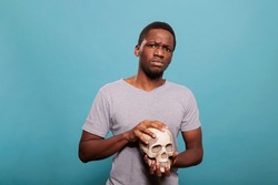 Millennial person holding human body skull from skeleton to study genetic bones for anatomy and biology knowledge. Anatomical and scientific subject to discover science education.