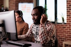 African american call center operator talking to clients on helpline, giving telemarketing assistance to people at customer care service. Helpdesk support consultant working at network reception.