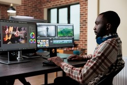 Digital footage professional editor at multi monitor workstation improving visual quality of content. Video editing expert sitting at desk in office workspace while digitally improving graphic project