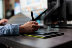 Closeup of creative graphic designer using stylus pen and graphic tablet to edit photos. Digital photo editor sitting at desk with multiple displays while using editing software to retouch images.