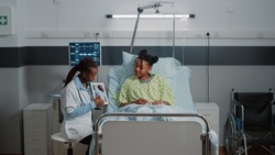 Medic holding tablet with cardiology figure to show diagnosis to woman in bed. Medical physician explaining cardiovascular exam results on device screen to sick patient. Healthcare checkup