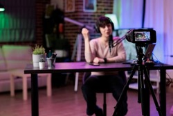 Young blogger recording online podcast discussion on camera, vlogging live channel content. Female influencer filming video conversation with audience, using streaming equipment.