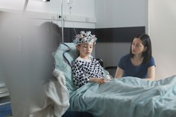 Neurology specialist examining neurological disease state of ill kid. Hospitalized sick girl wearing EEG headset resting in patient bed while doctor analyzing brain condition.