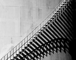 Heavy shadow of stairway on old white storage tank. Stairs cast interesting shadows in the late afternoon Sunlight. Black and White