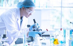 Asian woman scientist, researcher, technician, or student conducted research or experiment by using microscope which is scientific equipment in medical, chemistry or  biology laboratory