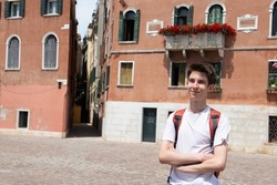 Handsome cheerful teen boy posing in the streets of ancient Venice with beautiful buildings at summertime