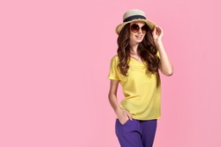 Young girl in sunglasses wearing, colorful clothes and straw hat, isolated over pink background.